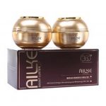 L’image montre deux pots ronds de couleur dorée au-dessus d’une boîte rectangulaire marron foncé. Les pots et la boîte sont étiquetés avec un texte blanc indiquant « AILKE ». L'emballage suggère que le produit est un produit de soin de la peau, éventuellement une crème ou une lotion.