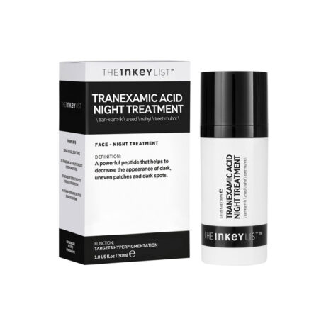 Une boîte blanche et noire du traitement de nuit à l’acide tranexamique The Inkey List est affichée à côté du flacon pompe à capuchon noir du produit. L'emballage prétend réduire les taches brunes et les taches inégales. La bouteille et la boîte contiennent toutes deux du texte en noir et blanc.
