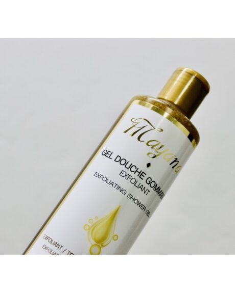 Gros plan d'une bouteille de gel douche exfoliant « Maya » au bouchon doré sur un fond blanc uni. L'étiquette indique « Gel Douche Gommant Exfoliant » et présente un motif de gouttelettes dorées.