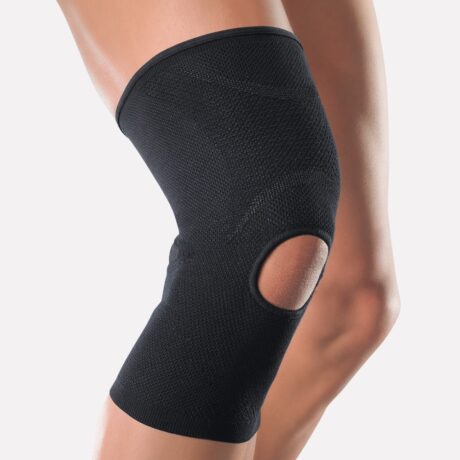 Image en gros plan du genou d'une personne portant une genouillère noire avec un motif rotulien ouvert. L'attelle couvre le genou et s'étend de quelques centimètres au-dessus et en dessous, offrant un soutien tout en permettant le mouvement. Le fond est blanc uni.