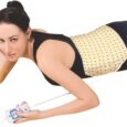 Une personne est allongée sur le ventre tout en tenant un petit appareil de commande. Ils utilisent un coussin chauffant abdominal qui entoure leur abdomen. Le coussin chauffant a un design simple avec un tissu de couleur claire présentant un petit motif.