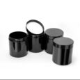 Quatre récipients cylindriques en plastique noir, trois avec couvercles fermés et un avec couvercle ouvert, disposés sur une surface blanche. Le couvercle du récipient ouvert est incliné vers l'arrière, révélant une doublure intérieure blanche.
