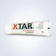 Un tube de dentifrice XTAR avec un capuchon blanc couché sur le côté sur un fond gris clair. L'emballage affiche « XTAR » en grosses lettres noires et « The Professional Toothpaste » en rouge. Des allégations telles que « blanchit les dents » et « combat les caries » sont imprimées sur le tube.