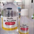 Deux flacons d'Huile de Paraffine de Valdafrique, un produit à usage médical, sont exposés sur une étagère. La plus grande bouteille est à gauche et la plus petite à droite. Les deux ont des capuchons blancs et des étiquettes jaunes comportant du texte rouge et noir en français.