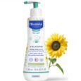Image d'un flacon blanc de crème émolliente Mustela Stelatopia avec distributeur à pompe, conçu pour les bébés et les enfants. La bouteille affiche des graphiques et du texte bleus et verts en plusieurs langues. Un tournesol jaune vif est positionné à côté de la bouteille.