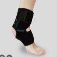 gros plan du pied et de la jambe d'une personne portant une chevillère noire. l'attelle a un talon ouvert et est fixée avec des bandes velcro, offrant une compression et un soutien à la cheville. l'arrière plan est gris clair uni.