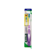 une brosse à dents gum emballée avec un manche violet et blanc. l'emballage est principalement vert et blanc, et comporte du texte sur les caractéristiques de la brosse à dents et le nom de la marque.