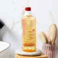 un flacon d'huile nettoyante réparatrice topicrem da protect avec un distributeur à pompe est posé sur le comptoir d'une salle de bain. derrière lui se trouvent une brosse à cheveux et un peigne dans un récipient. la scène suggère une salle de bain propre et minimaliste.