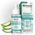 un produit garnier skin naturals est doté d'un flacon compte gouttes d'acide hyaluronique et d'un super sérum repulpant à l'aloès. le flacon en verre se trouve à côté de sa boîte, qui comprend les détails du produit et des images d'aloe vera, accompagnées de feuilles d'aloès en arrière plan.