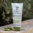 un tube de gommage corporel le petit olivier est posé sur une surface en pierre à l'extérieur, entouré de branches d'olivier. l'emballage comporte des images d'olives et un texte indiquant les ingrédients naturels et la formule sans sulfate.