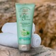 un tube d'après shampoing le petit olivier à l'aloe vera et au thé vert, étiqueté sans silicone. l'emballage vert menthe est posé sur une serviette blanche pliée sur un fond de roche naturelle floue.