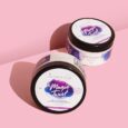 deux contenants ronds de crème au beurre « magic twist » sont posés sur une surface rose. les contenants ont des couvercles noirs et des étiquettes blanches avec du texte violet et bleu. l'étiquette indique « ultra nourrissante » et « le secret de loly ».